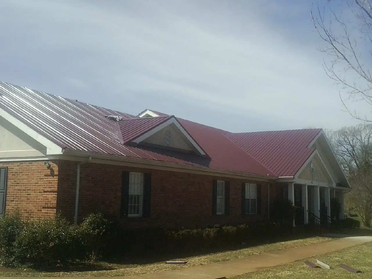 Red metal roof with gabled entries on a long brick building, from a Hail Damage Roof Repair job in Rayne
