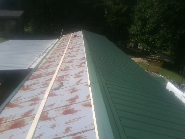 Old rusted panels beside newly installed green metal roofing — Wind Damage Roof Repair by Roofing Brothers in Rayne