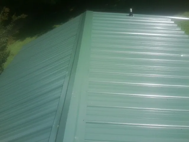 New green metal panels meeting at the ridge of a roof — Flat Roof Repair work by our crew in Rayne