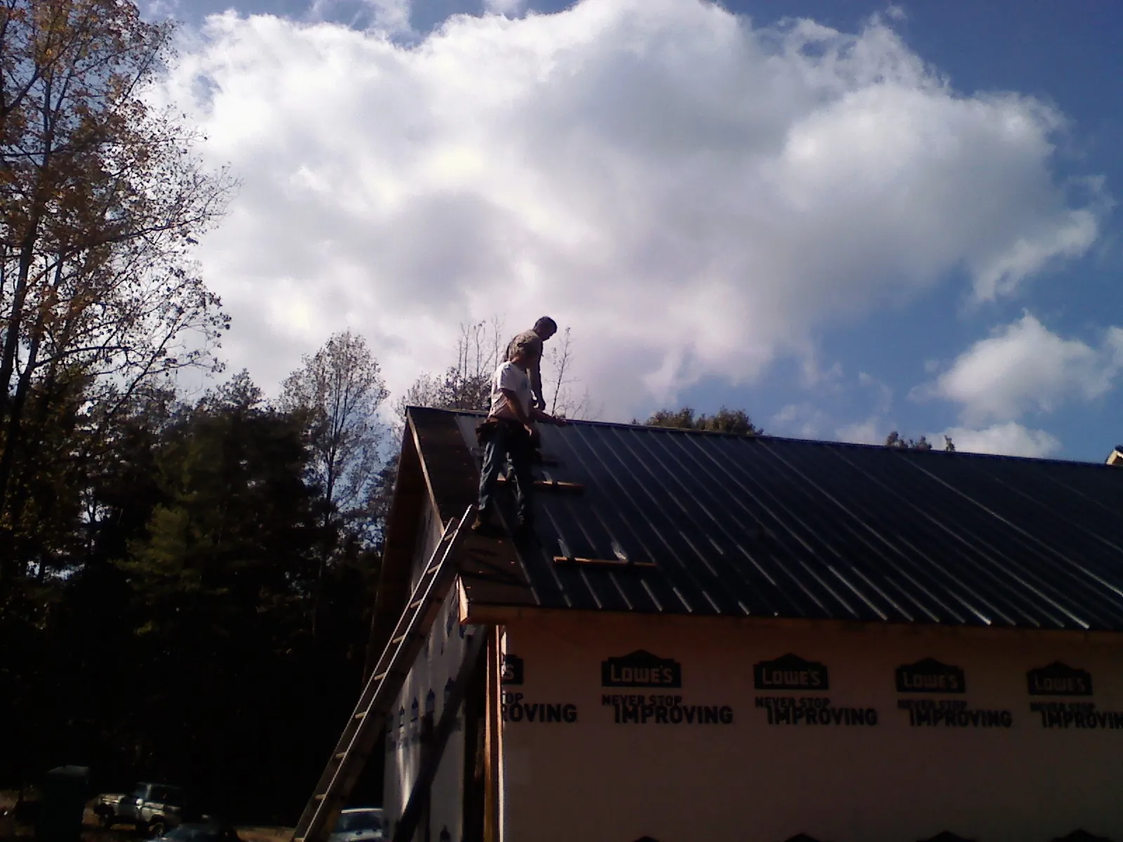 Roofer fastening dark metal panels high against a cloudy sky, from a Roof Inspection job in Rayne