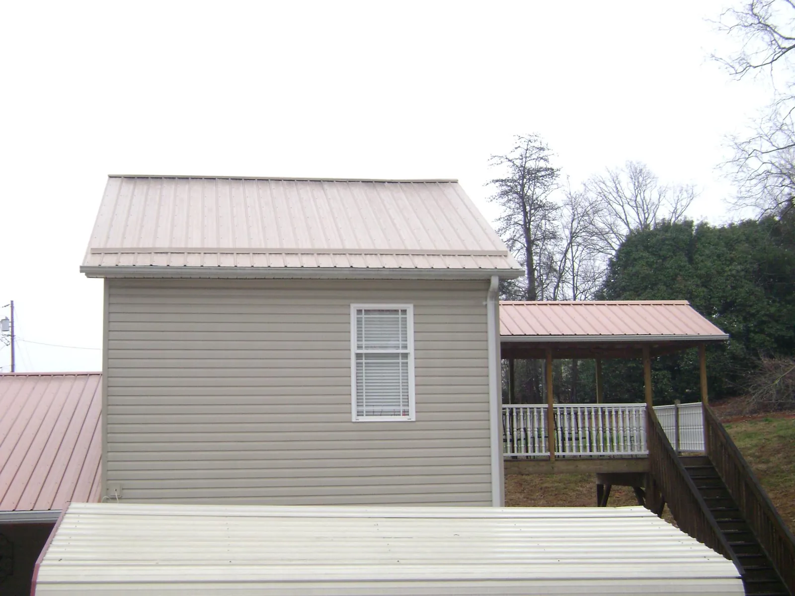 Tan metal roofs on a two story addition and attached porch, from a Roof Replacement job in Rayne